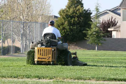 A man mowing a large field in a riding lawnmower.