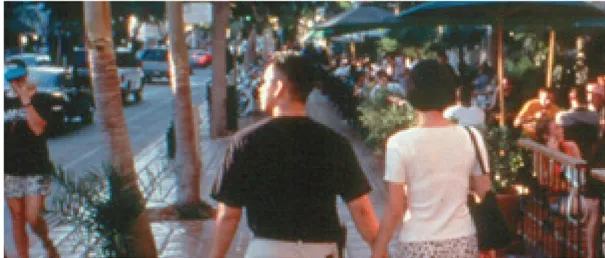 A couple walking down a busy street with outdoor patios.
